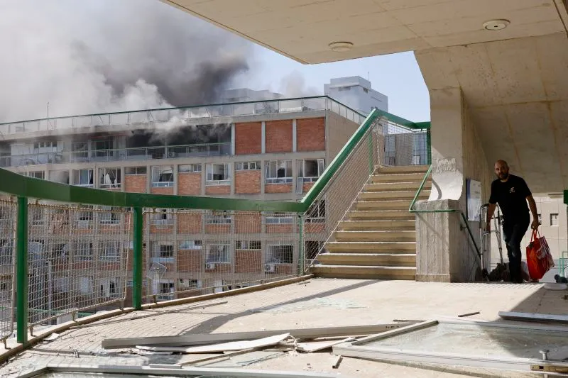 A man carries bags as smoke billows from a building at Soroka Hospital in Be'er-Sheva on Thursday.