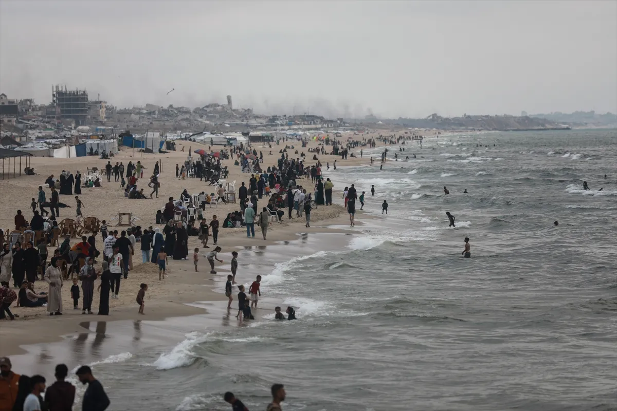 people gather on a sea shore near tents as smoke rises in the distance
