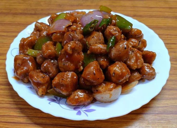 This may contain: a white plate topped with meat and vegetables on top of a wooden table next to a fork
