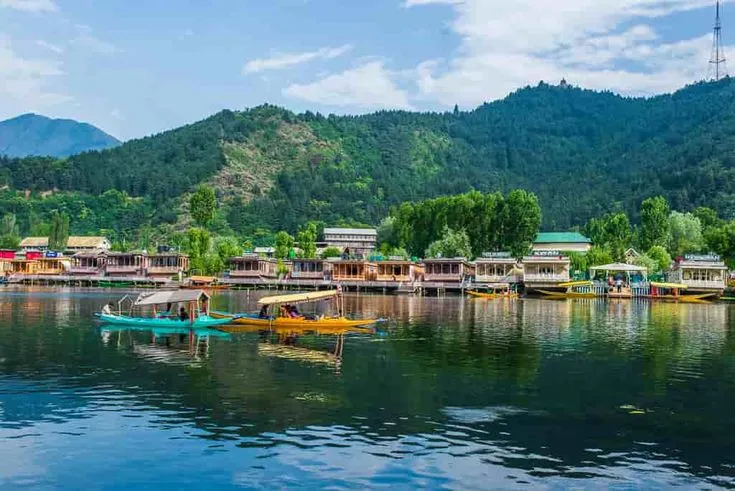 This may contain: there are many small boats on the water in front of some houses and mountains behind them