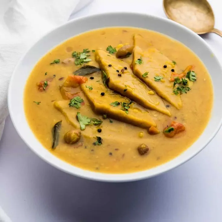 This may contain: a white bowl filled with soup and some spoons