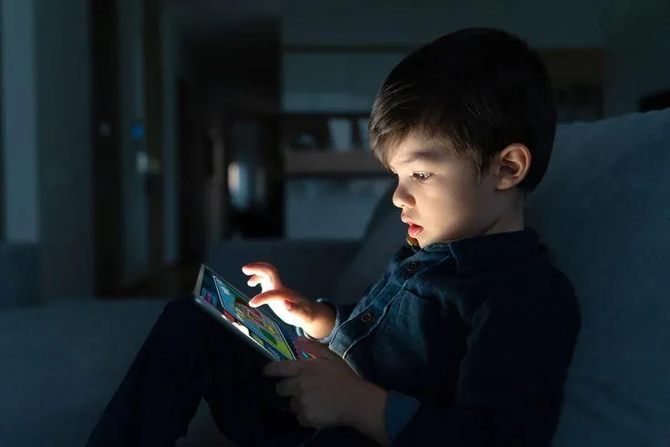 This may contain: a young boy sitting on a couch looking at an electronic device in his hands,