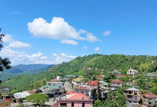 This may contain: a hill with houses on it and trees in the foreground, surrounded by mountains