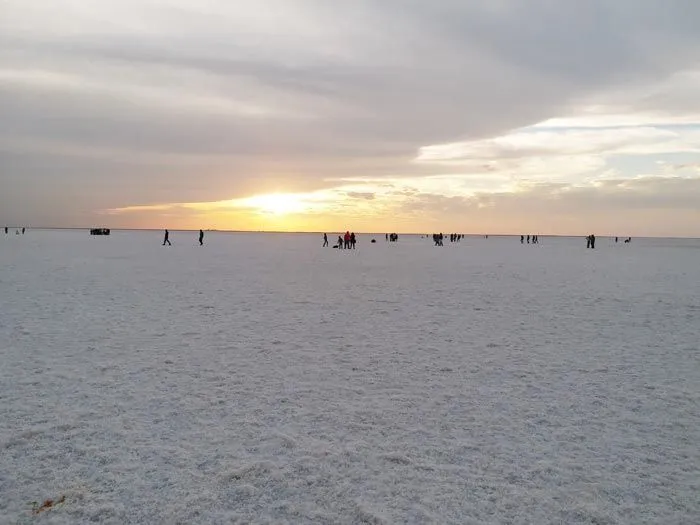 This may contain: the sun is setting over an expanse of sand with small boats in the water and people walking on it