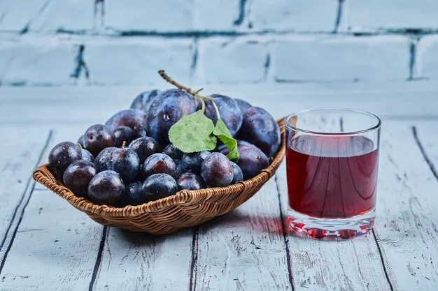 Free photo garden plums on basket on blue with a glass of juice.