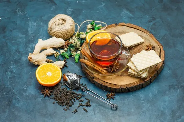 Free photo tea with herbs, orange, spices, waffle, thread, strainer in a mug on wooden board and stucco background, flat lay.