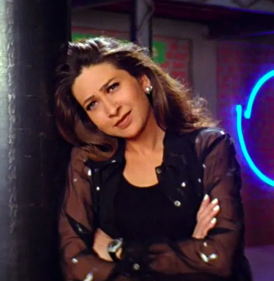 This may contain: a woman leaning against a pole in front of a neon sign with her arms crossed