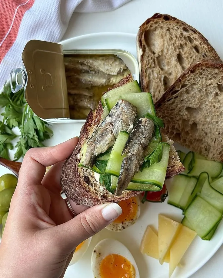 This may contain: a person is holding up a sandwich with cucumbers, tomatoes and bread on it