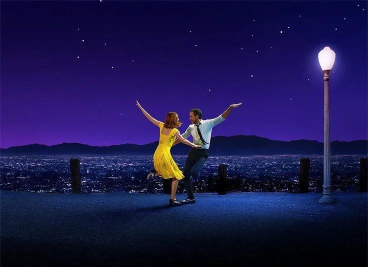 This may contain: a man and woman dancing in front of a city at night with the lights on