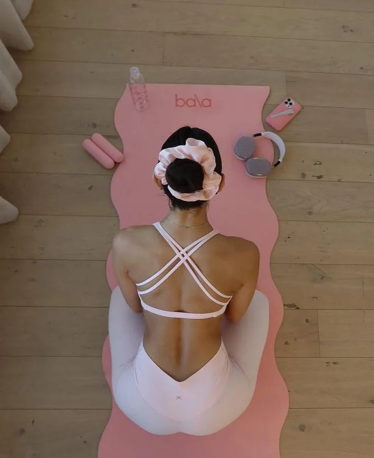 This may contain: a woman sitting on top of a pink mat with her back turned to the camera