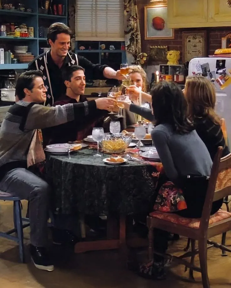 This may contain: people sitting around a table toasting with wine glasses