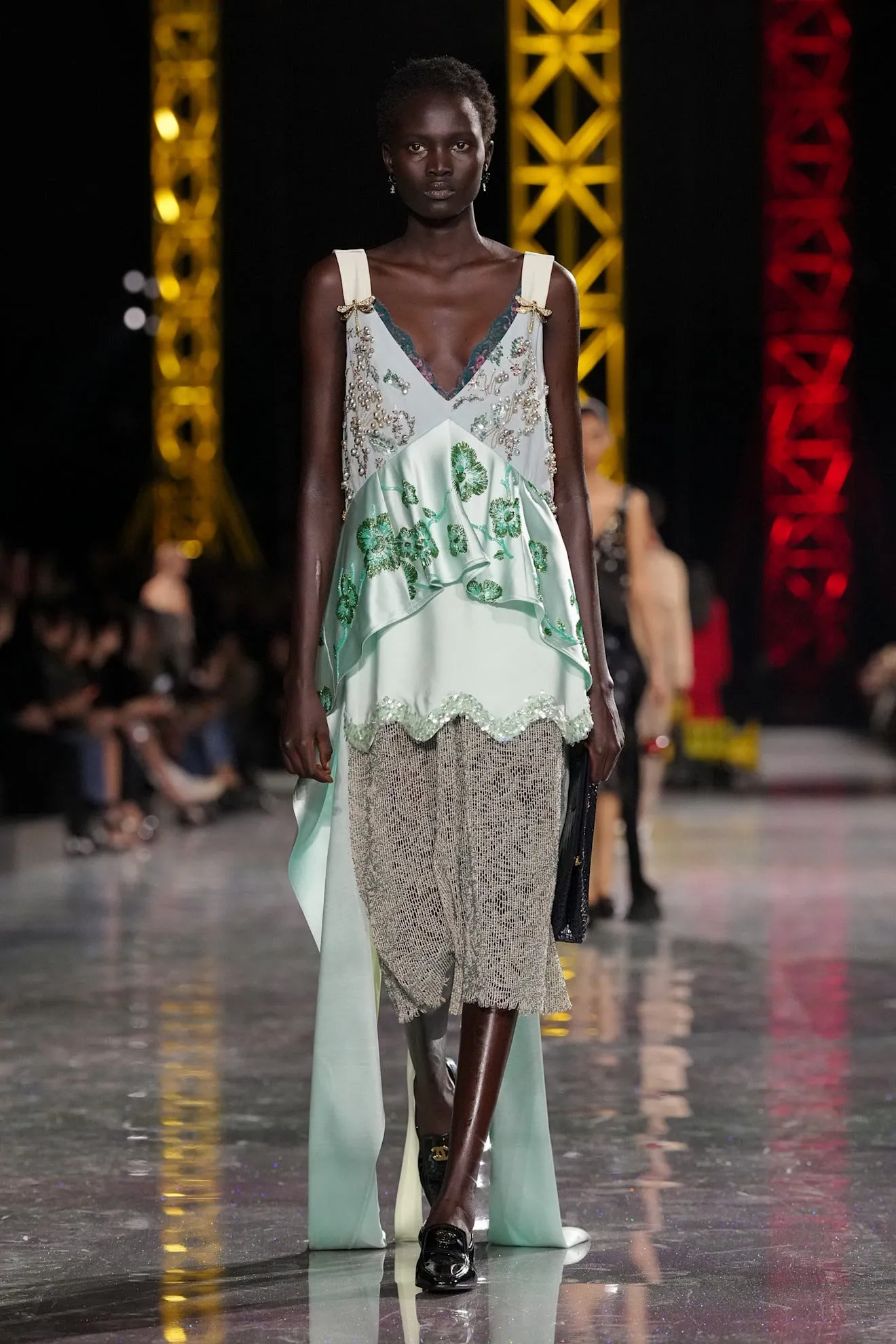 Model walking in a fashion show wearing a layered outfit.