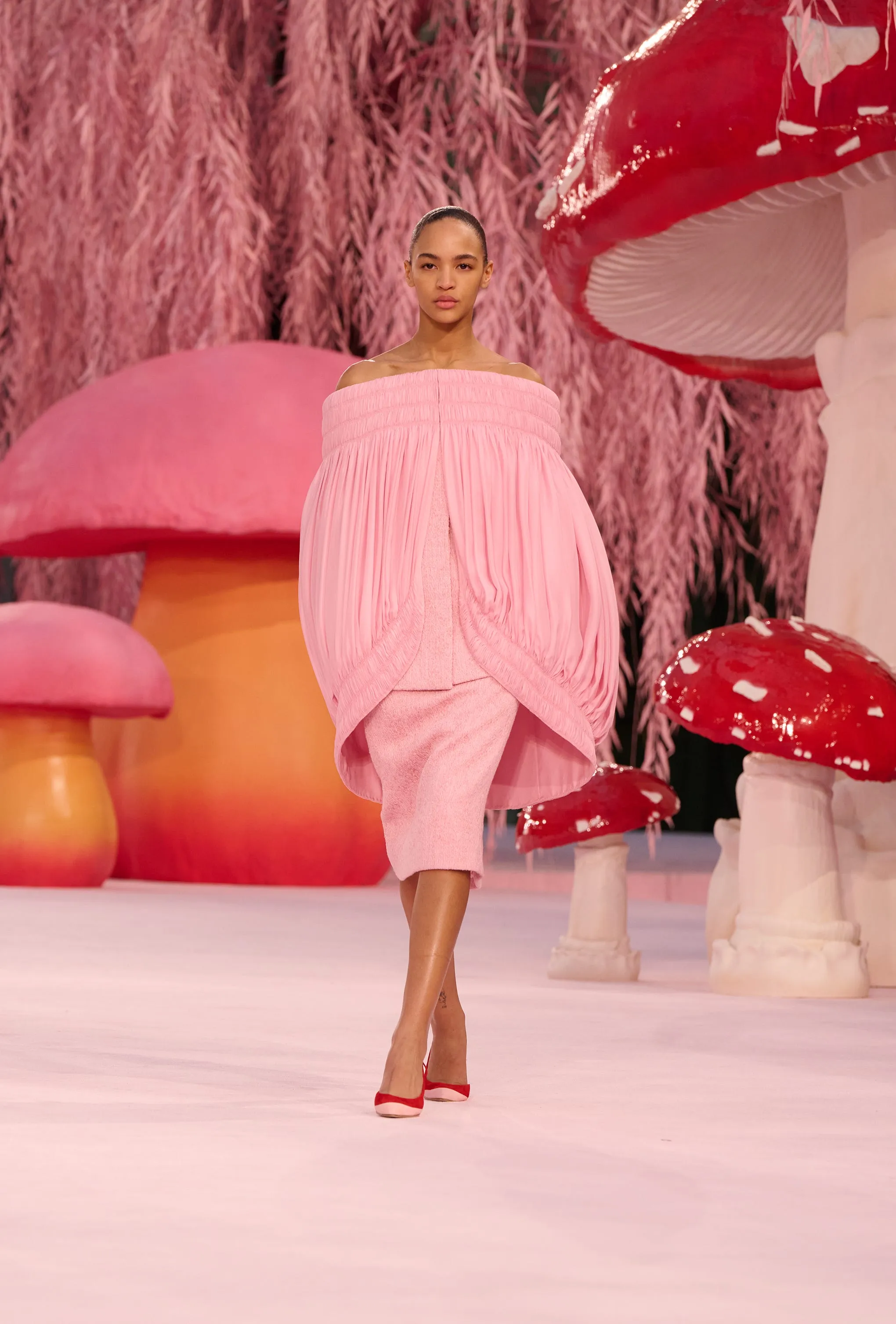 Fashion model walking on a runway with colorful mushroom props.