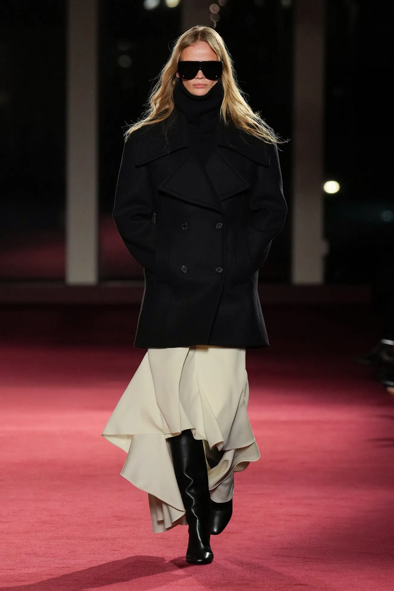 Fashion model walking on runway wearing a stylish outfit with a coat and skirt.