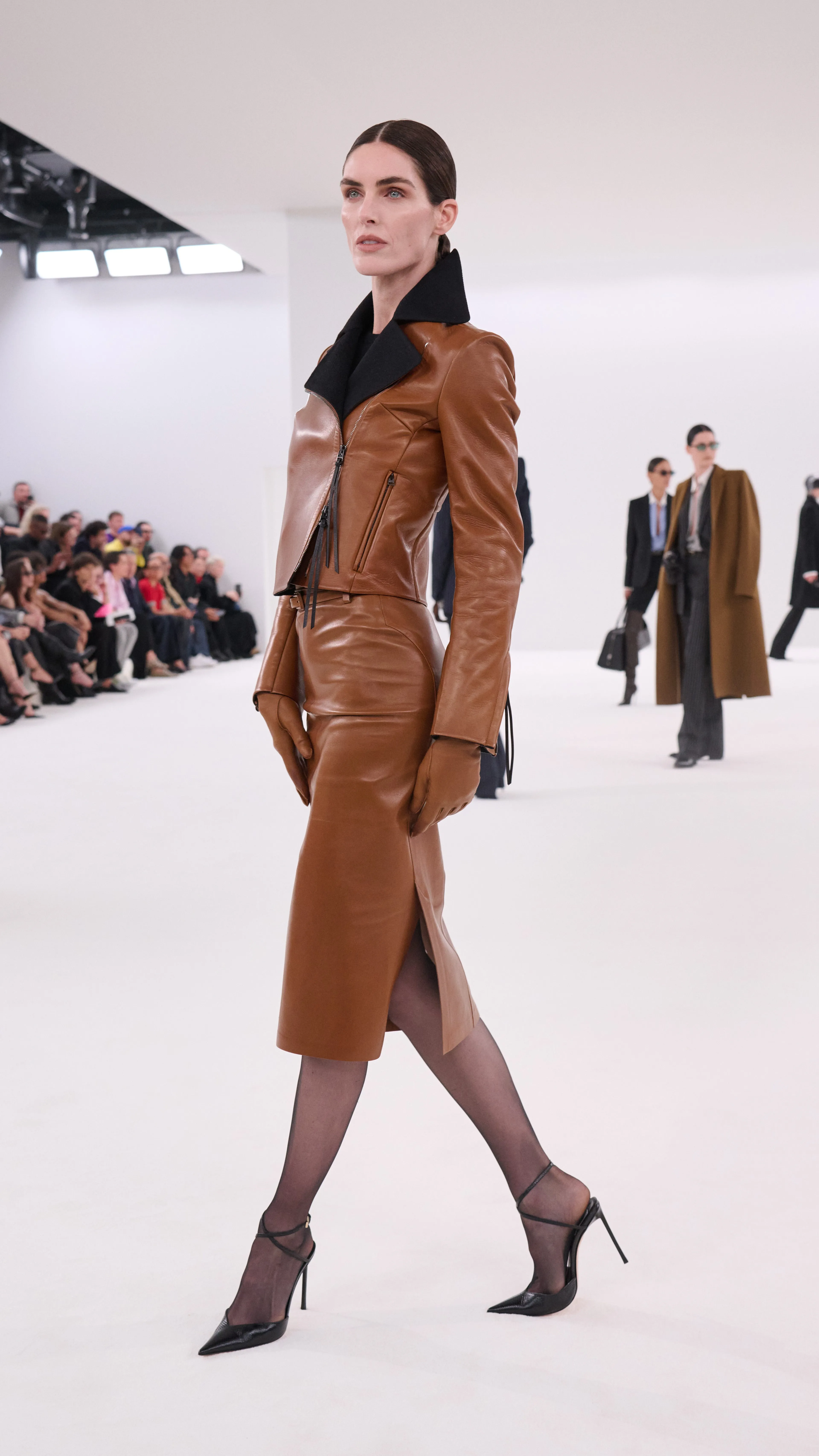 Fashion model walking on a runway showcasing a leather outfit.