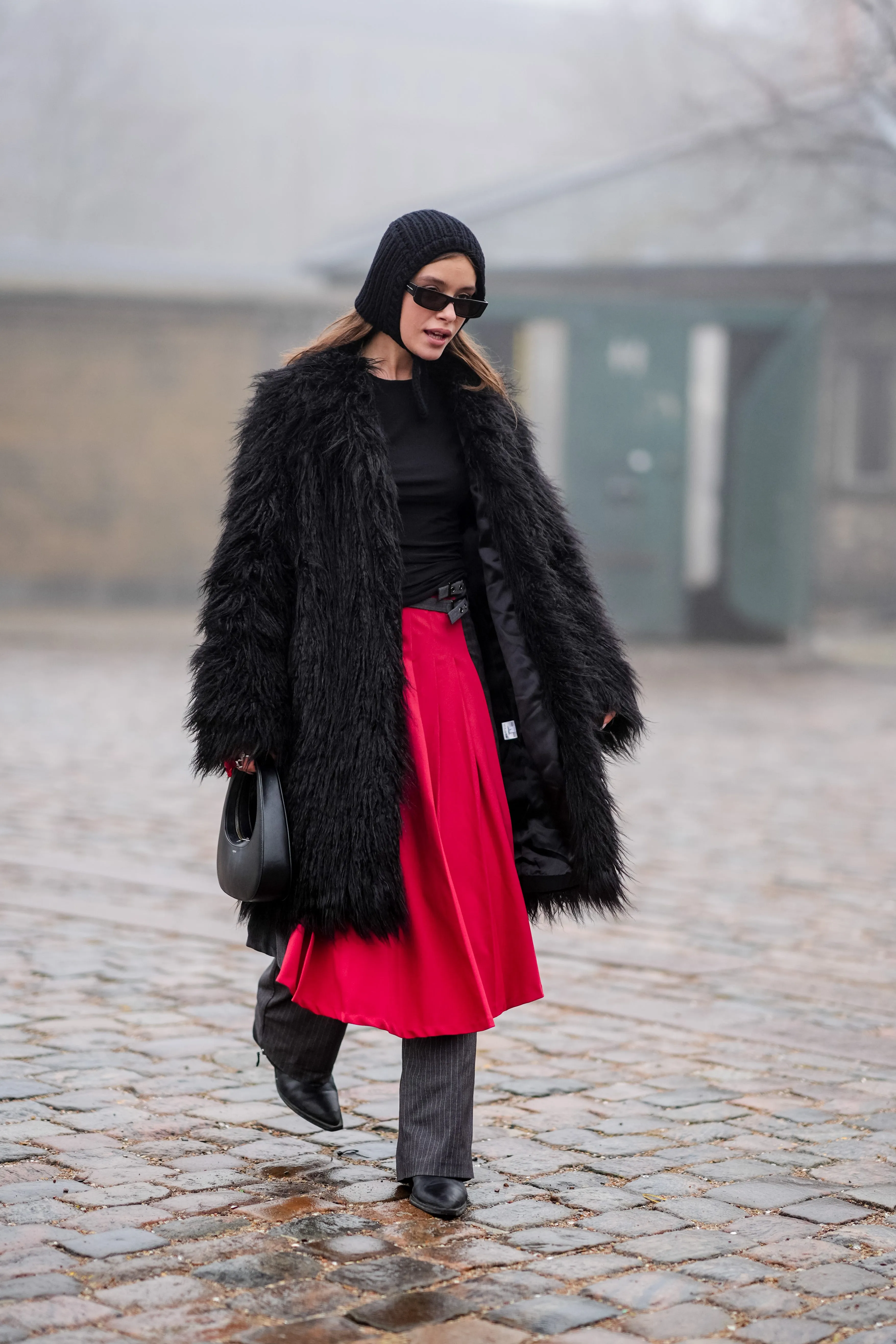 copenhagen, denmark january 30: a guest wears a ribbed wool hood sunglasses, a black fluffy long coat, a black leather coperni bag, a red skirt, gray striped flared pants, black leather pointed shoes, outside rolf ekroth, during the copenhagen fashion week aw24 on january 30, 2024 in copenhagen, denmark. (photo by edward berthelot/getty images)