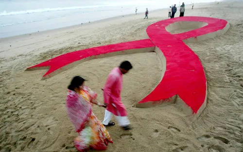 An Indian couple walk past a 50 foot (15.24 meter) long AIDS red ribbon sand sculpture, created by Sudarshan Pattnaik on World AIDS Day in Puri, India, Monday, Dec.1, 2008. (AP Photo/Biswaranjan Rout)