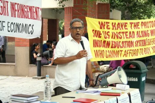 A person wearing white shirt standing with a mic. In the background, there is college campus with some students sitting. A yellow banner with incomplete lines 