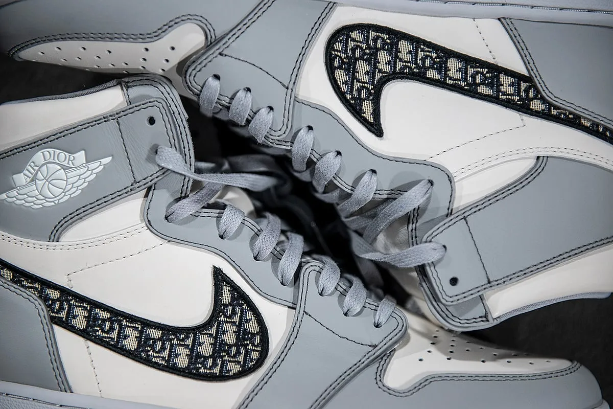 Dior X Air Jordan 1 High SneakersMeticulously crafted from premium wolf grey and sail white leather, these sneakers embrace the iconic high-top silhouette while introducing a contemporary twist through a grey-hued Dior monogram swoosh. 