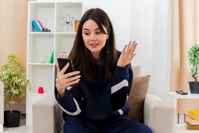 impressed-young-pretty-caucasian-woman-sitting-armchair-designed-living-room-holding-looking-mobile-phone-keeping-hand-air Medium