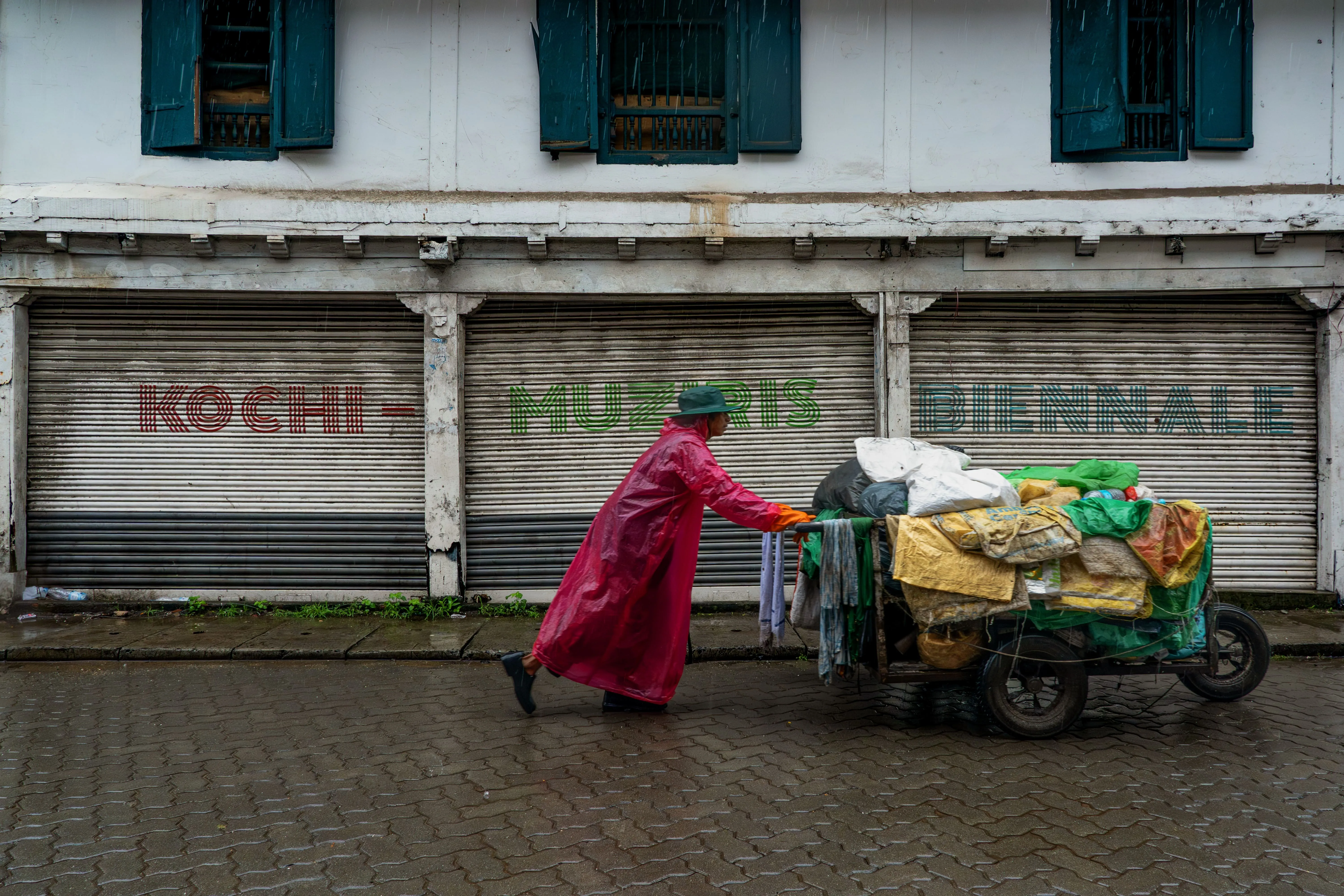 A man pushes his cart past a wall bearing Biennale lettering in Mattancherry (1)