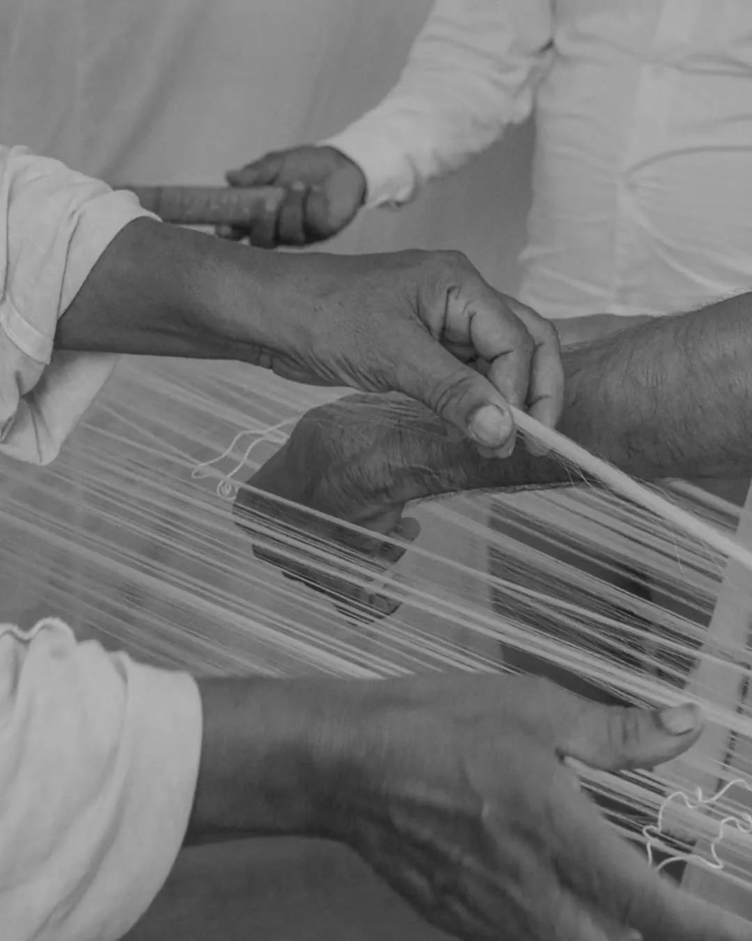 Warp preparation, in frame, hands holding generations of skill. A quiet tradition, shaping a mo