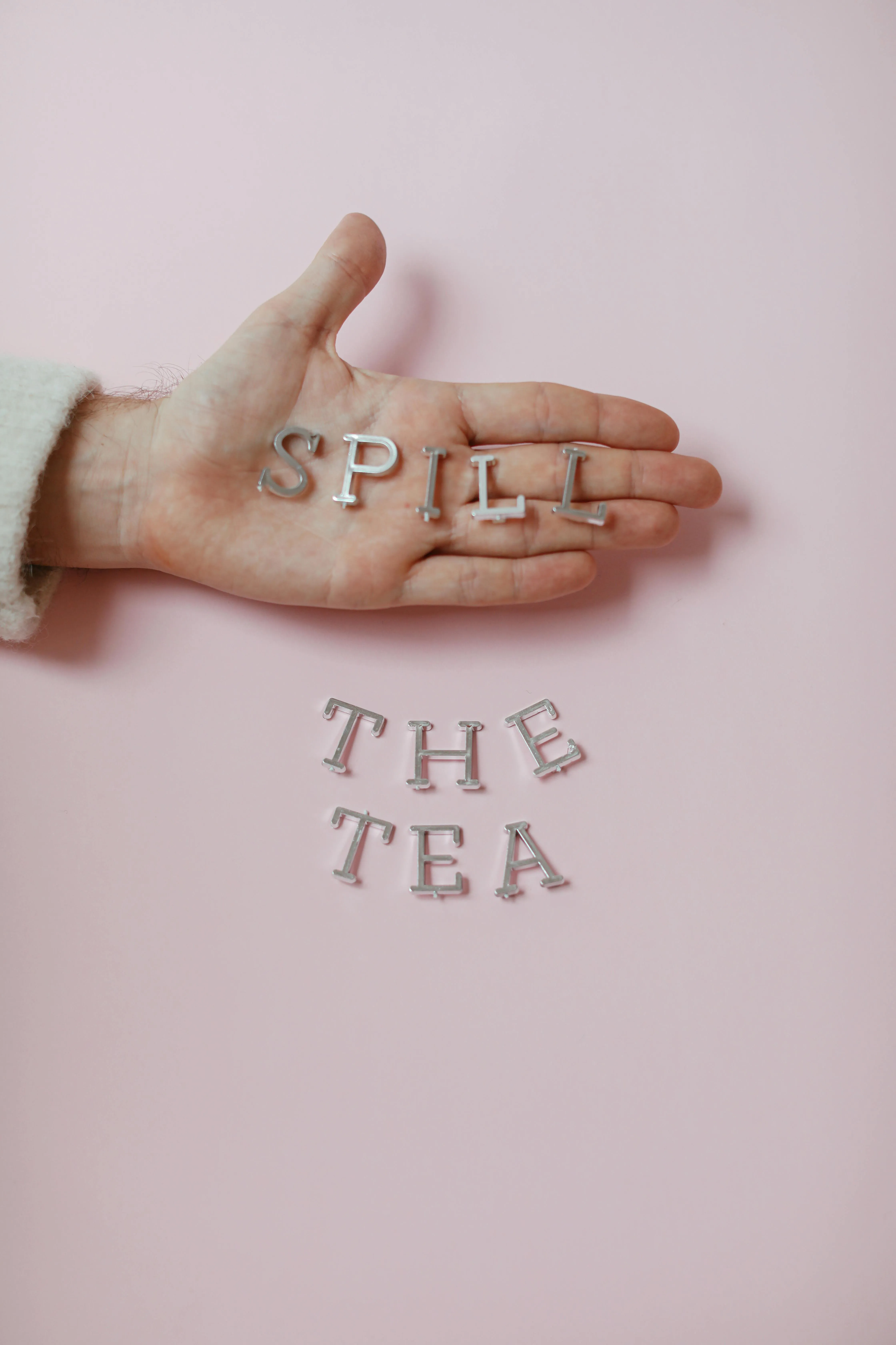 A picture of a hand and silver alphabets spelling out Spill The Tea