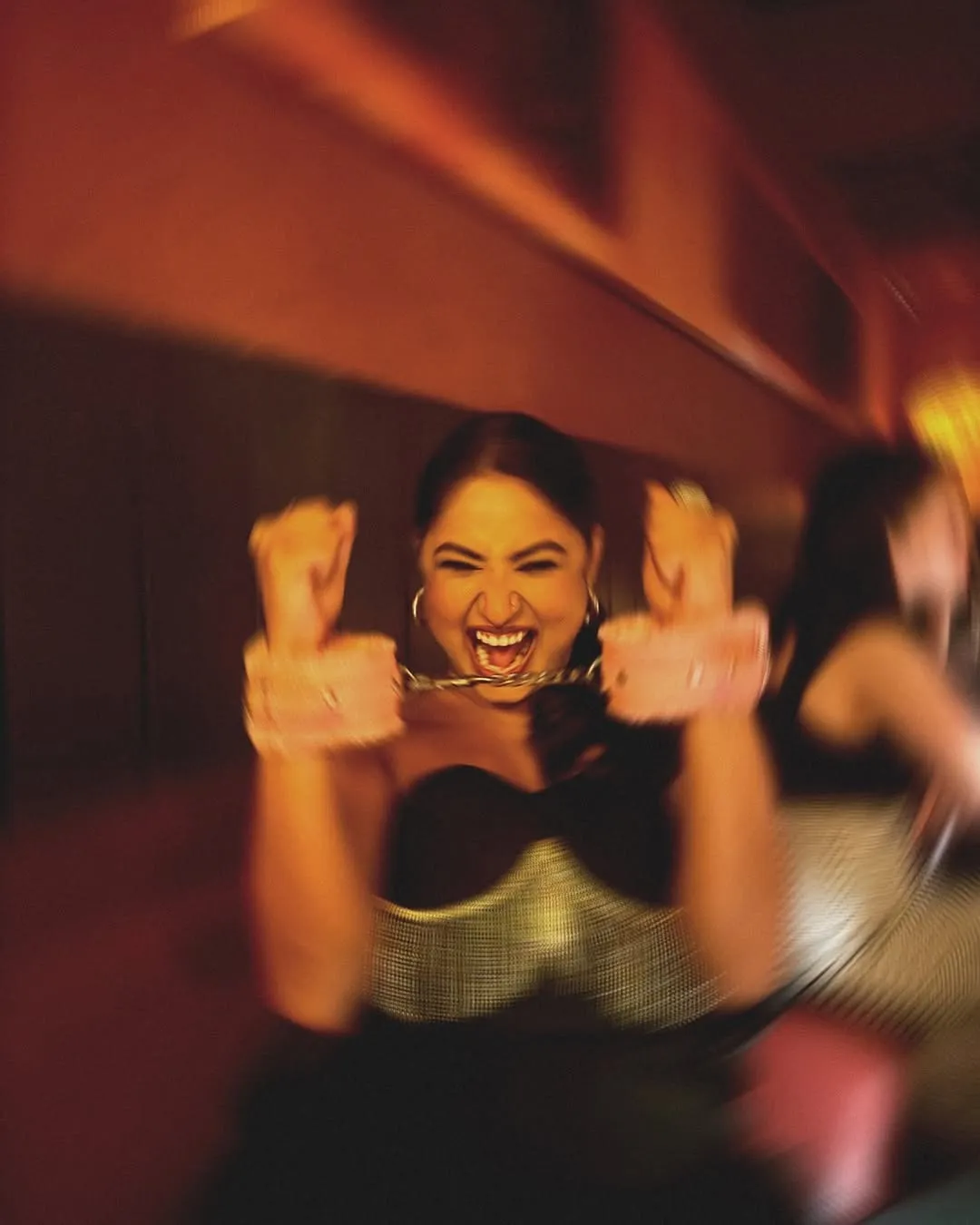 A woman smiling  playfully while  wearing pink  handcuffs at a  nightlife event,  celebrating India’s  playful and open  approach to kink