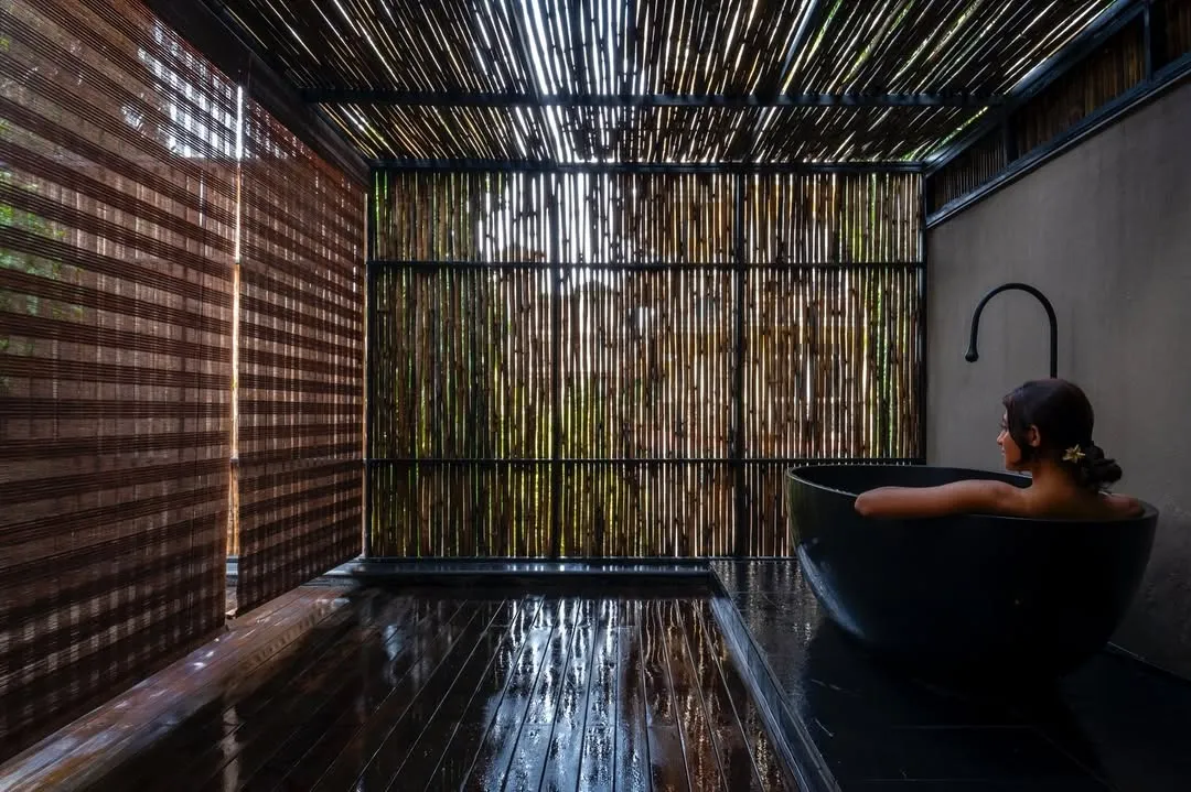 A woman sits in a bathtub in Amaraanth, Goa, one of the eco resorts in India that focuses on being one of the sustainable hotels India, with tastefully done bamboo panelling and woodwork making it one of the luxury resorts India.