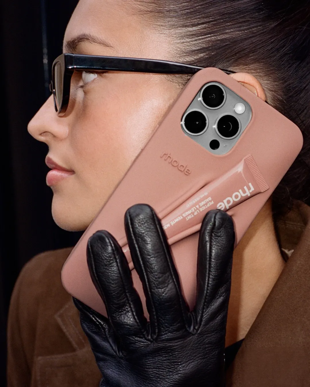 Rhode's phone case with lip balm in a woman's hand with black gloves, reflecting the lifestyle-ification of beauty products