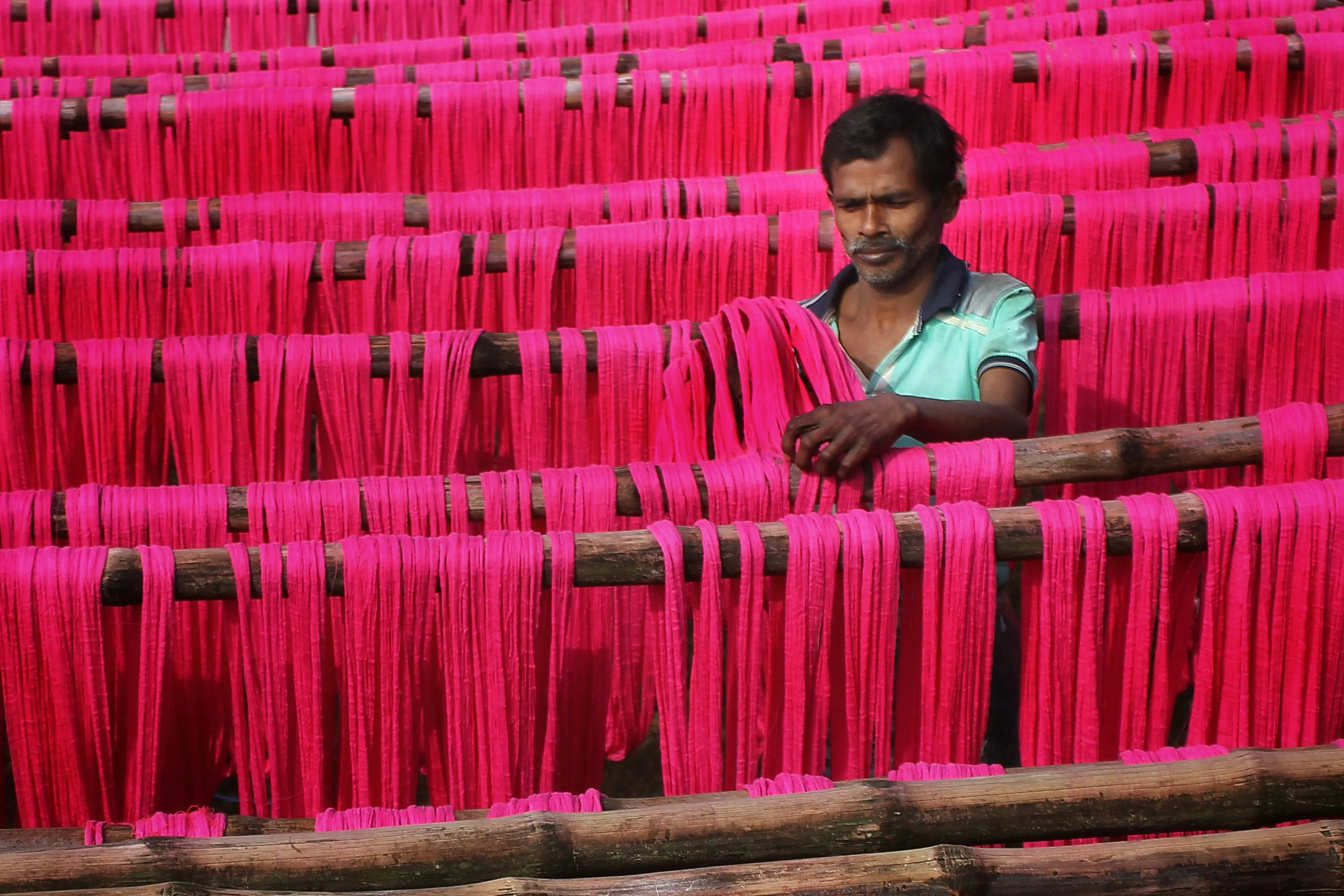 A picture of a man working with pink weaves to show how the immigration paradox within India's textile industry to highlight the root of anti immigration protests