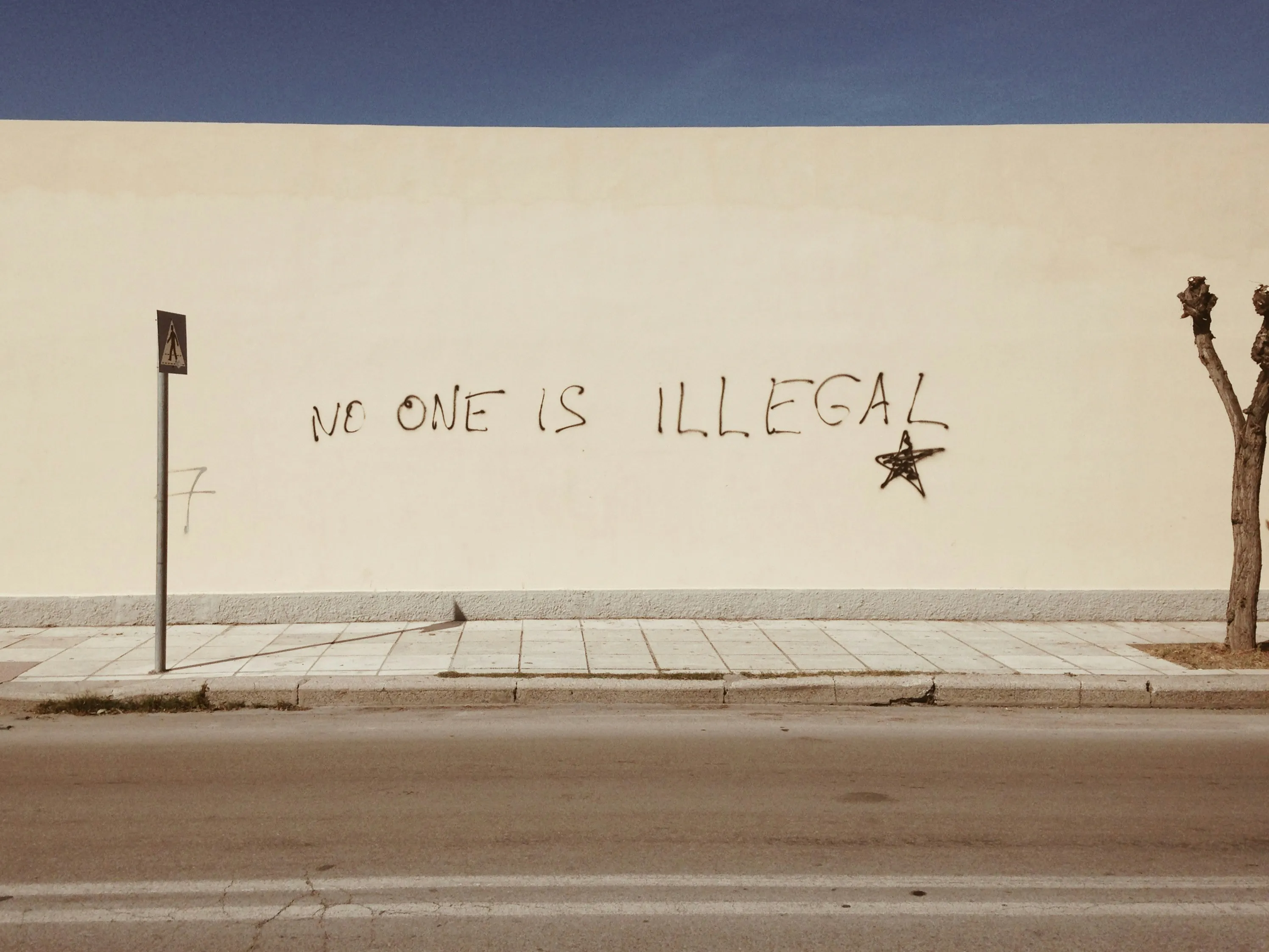 A picture of a yellow wall with the words 'no one is illegal' drawn on it to depict the anti immigration protests which also involves Indian immigrants