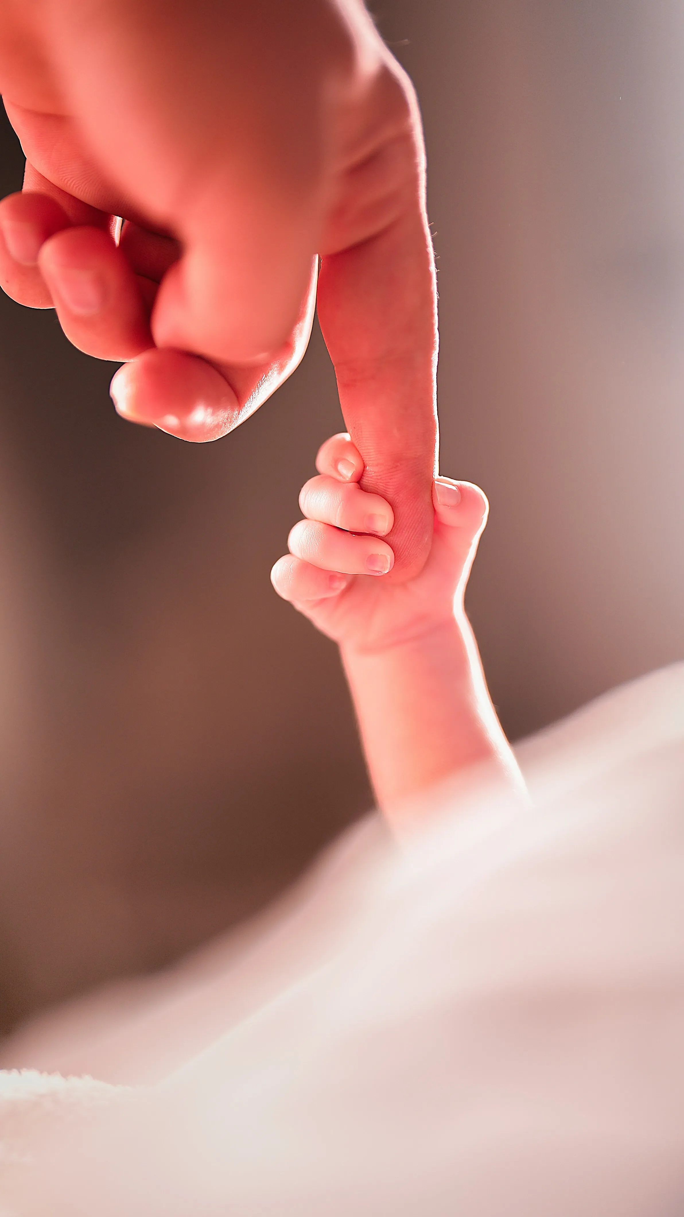A picture of an adult person's finger being held by a new born baby's hand to depict the rise of queer parenting in India and raising kids in queer families, despite incompatible surrogacy laws for queer couples India