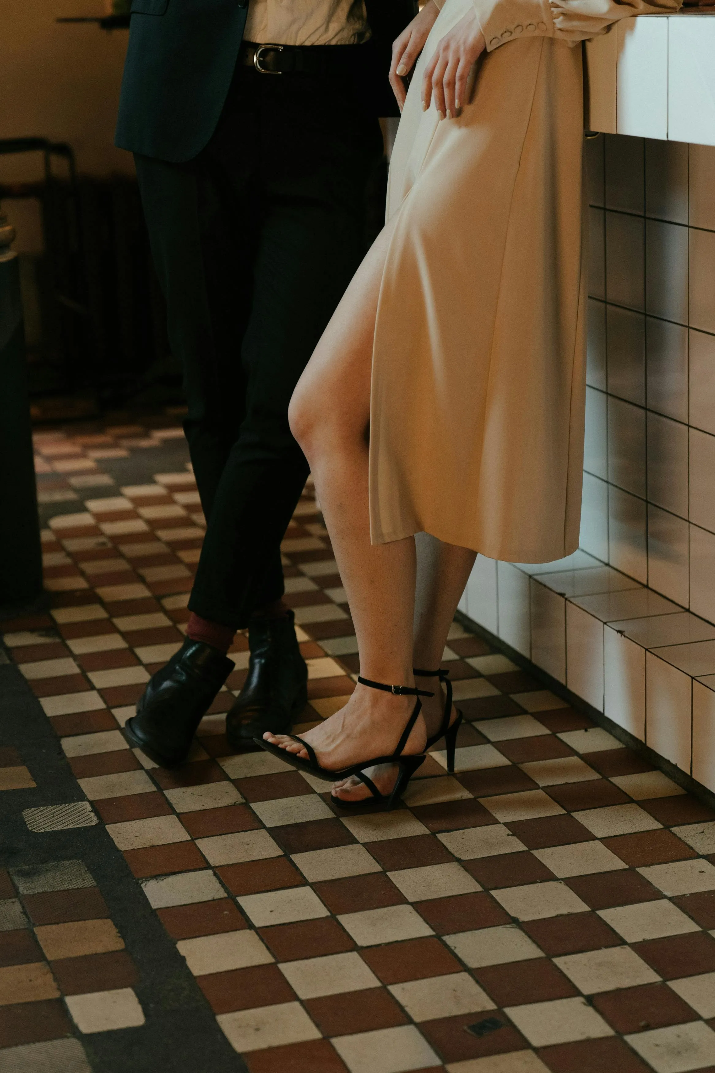 A picture of the lower halves of a couple-a woman in heels and a dress with a slit and a man wearing shoes and pants, belt, shirt and a coat-to depict now making the effort or knowing how to plan a first date as one of the primary first date red flags that people tend to overlook due to the current dating app culture India