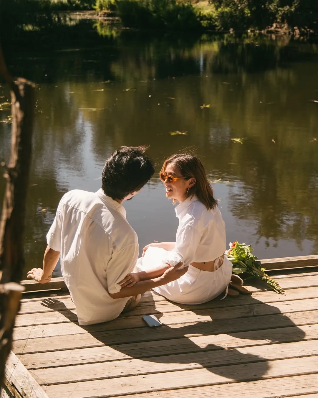 A man and woman sitting by the lake on a wooden boat
