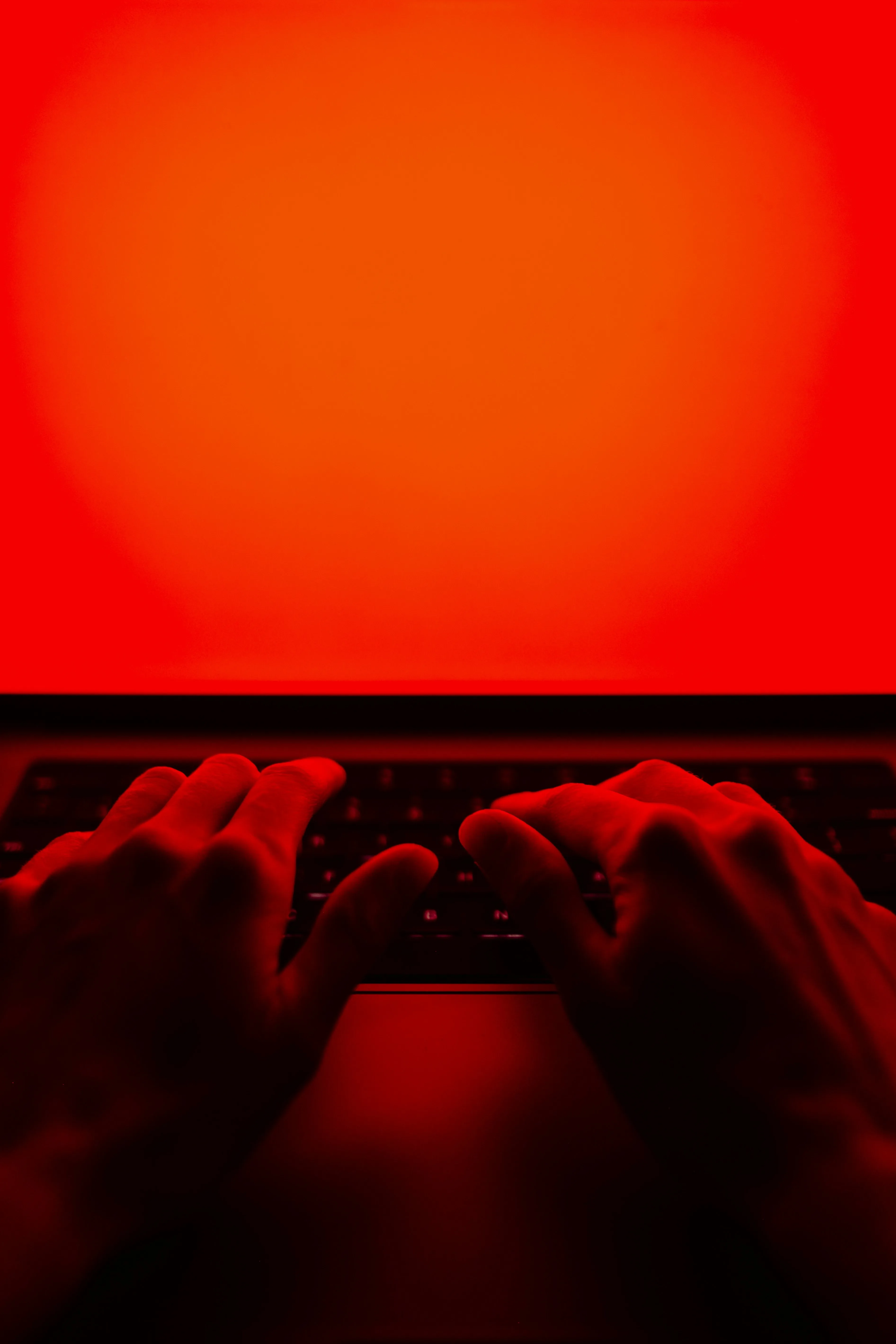 A picture of a person's hands on a laptop with a red screen in red light to show how rage baiting in marketing works due to the rise of social media outrage