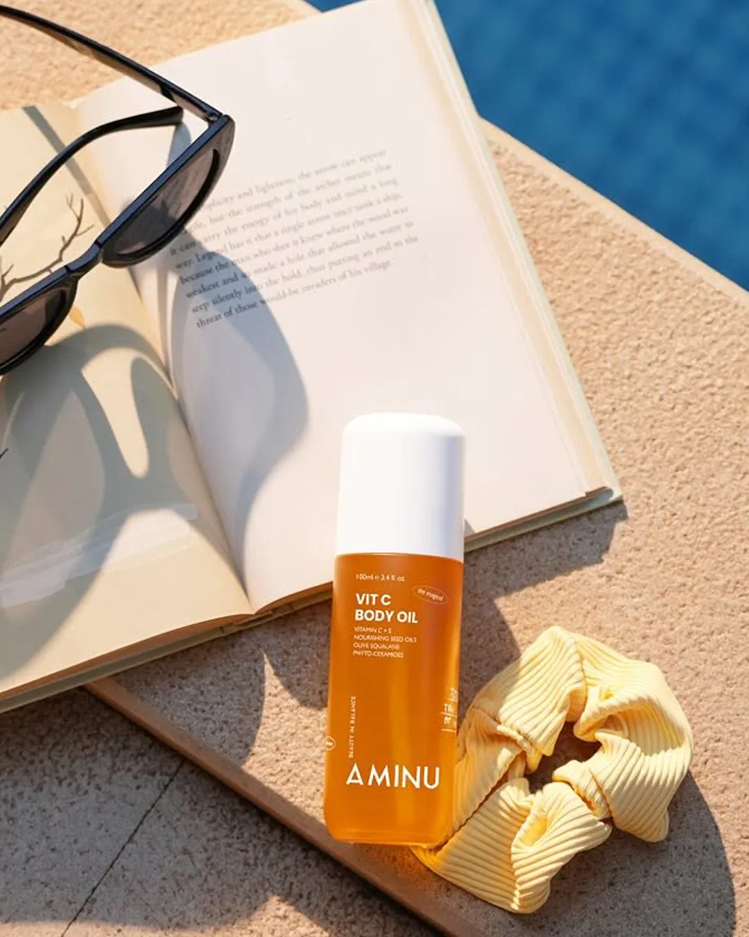 Body oil products India from Aminu placed on a book by the swimming pool