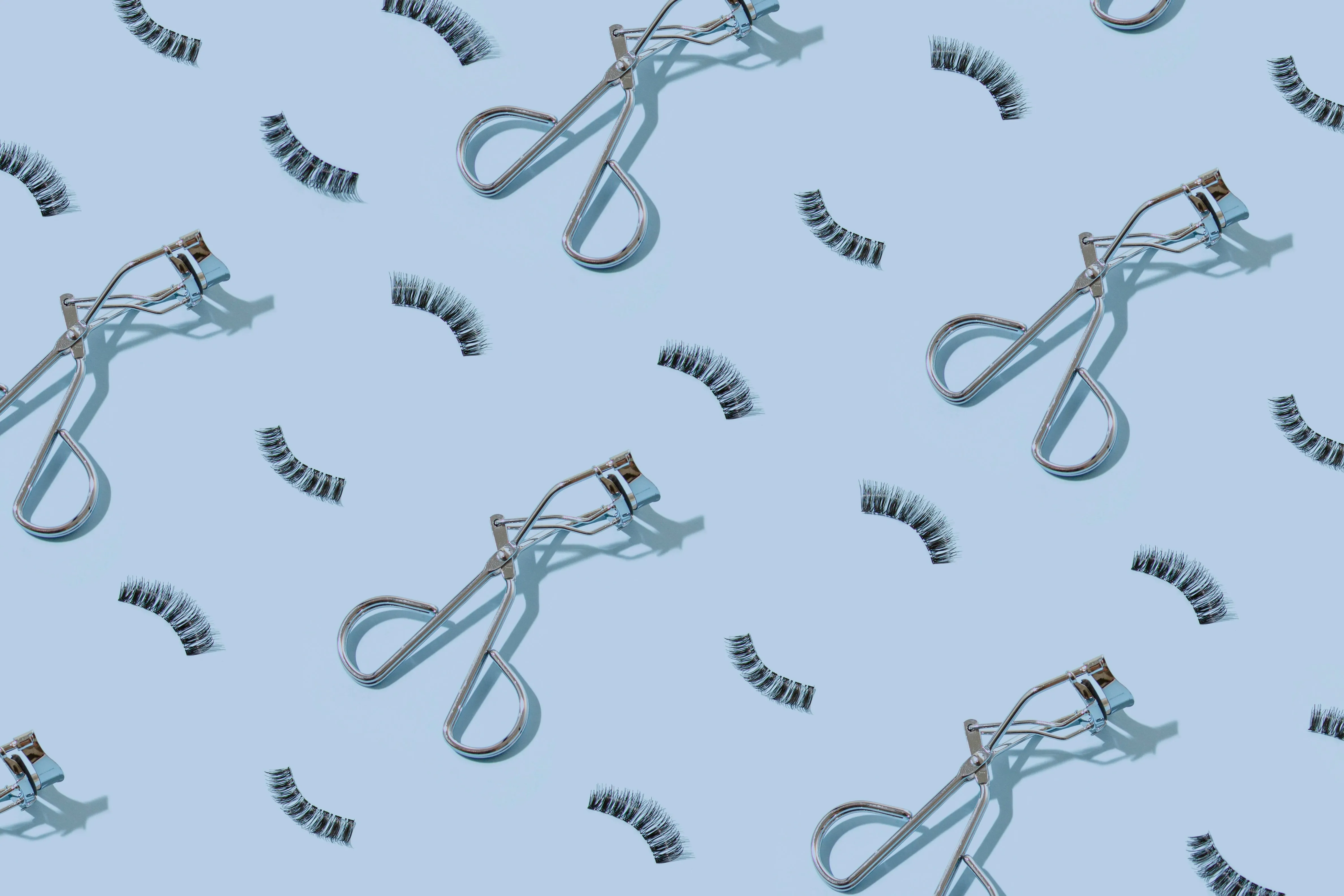 Flatlay shot of eyelash curler and falsies placed on a blue backdrop
