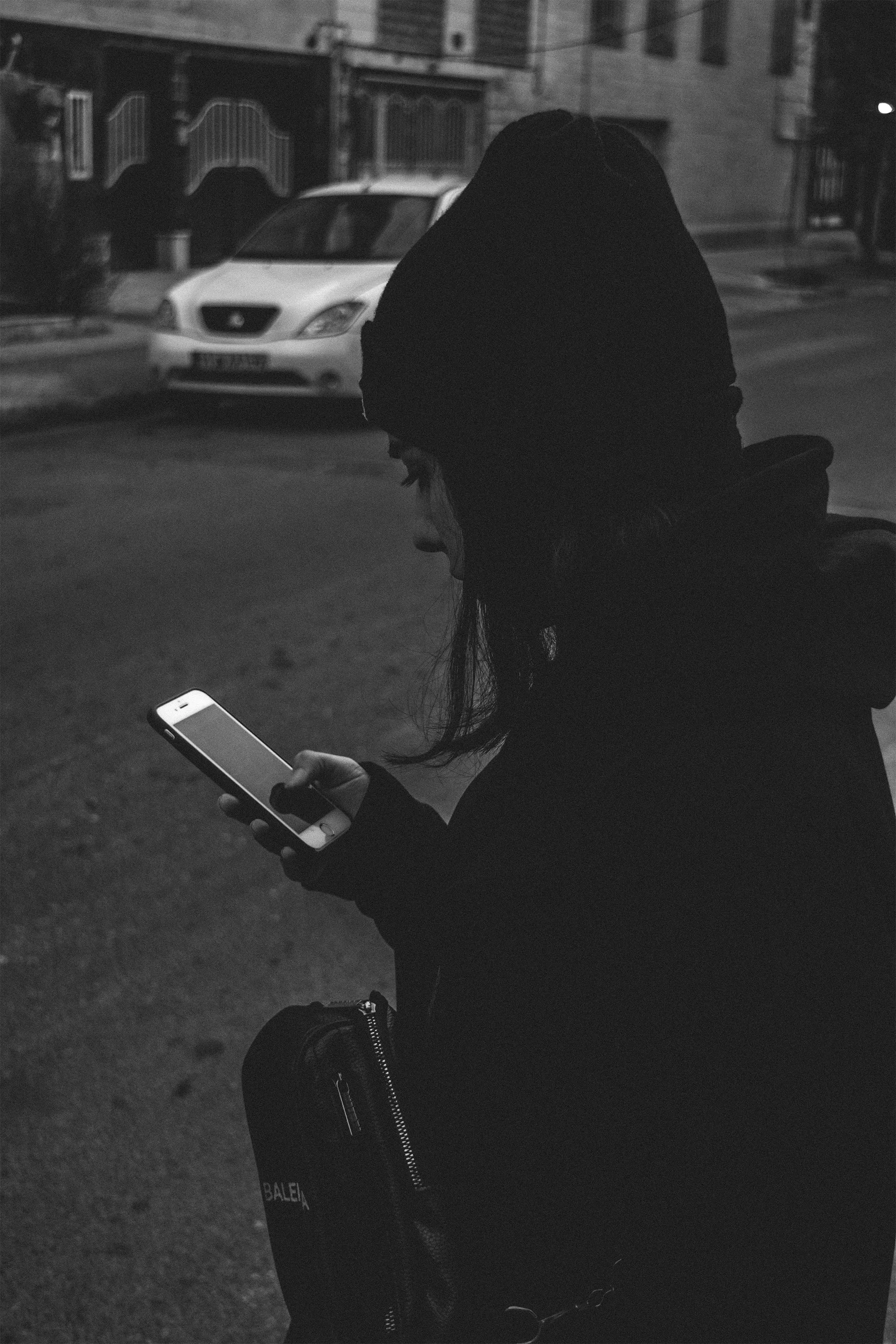 A black and white picture of a woman staring at her phone while wearing a beanie and standing on the road to depict the uncertainty that cushioning in dating brings to Gen Z relationships and the Indian dating culture