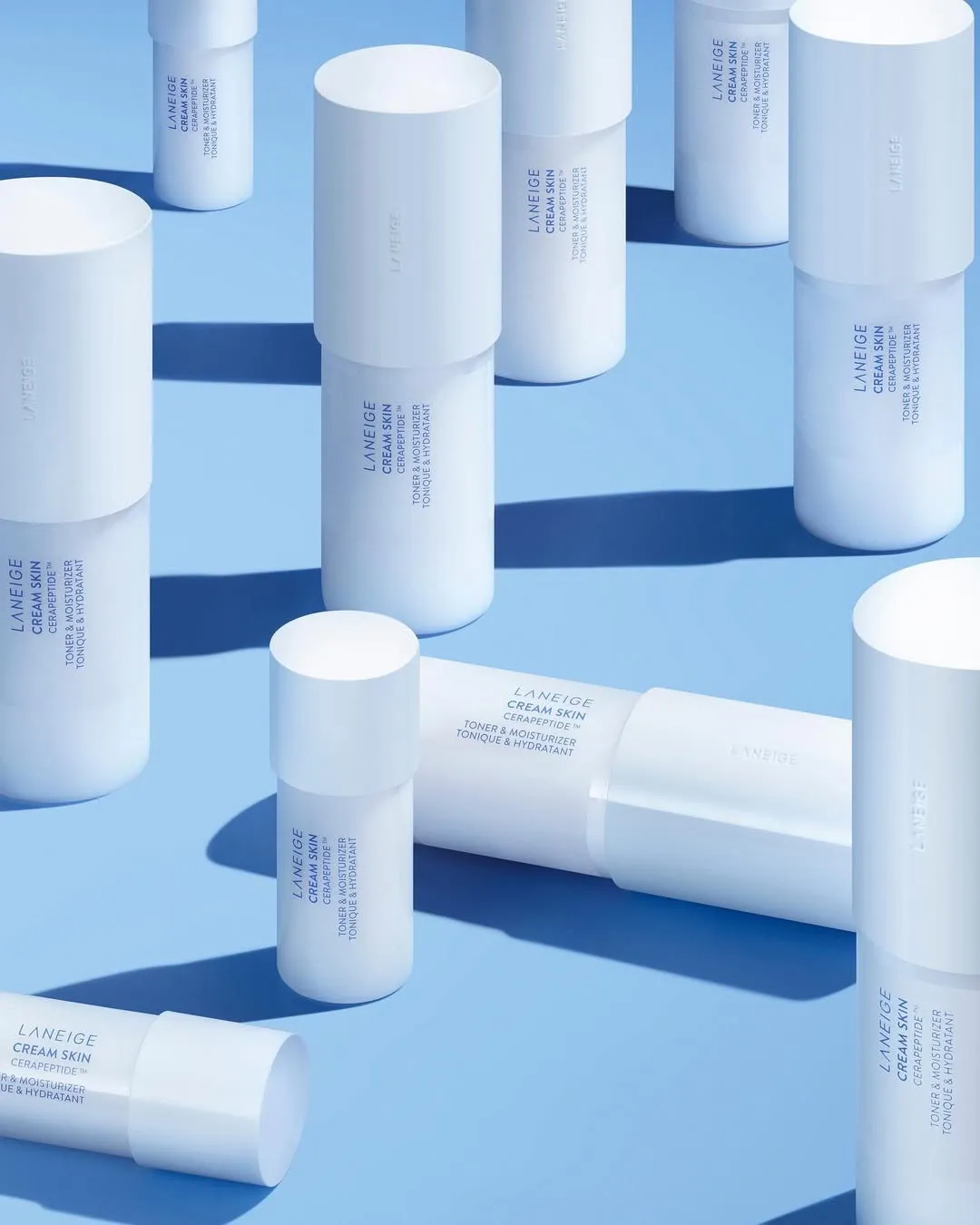 A few bottles of Laneige milky toners placed on a powder blue backdrop