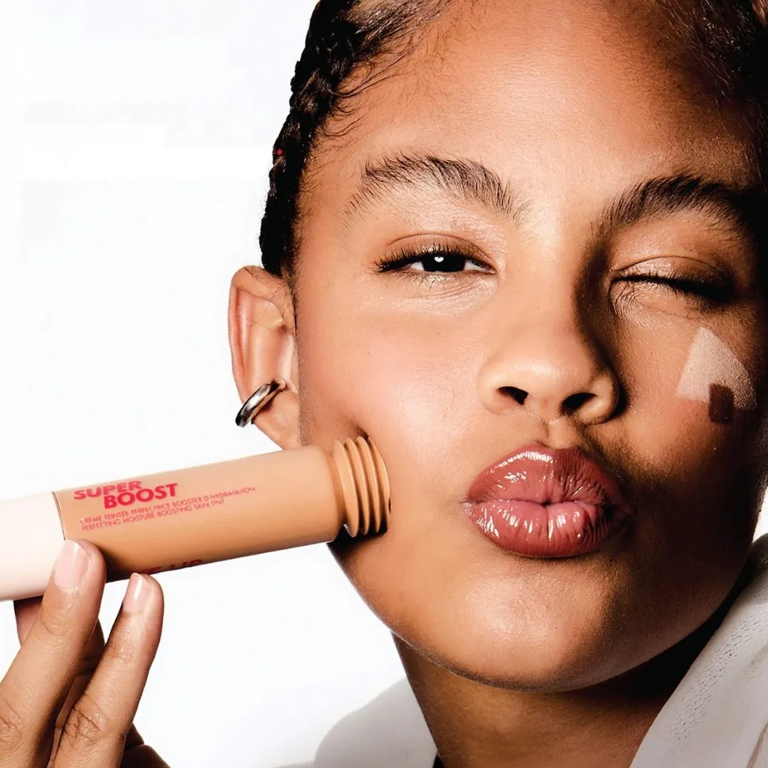 A female model pressing a tube of the skin tint against her cheek