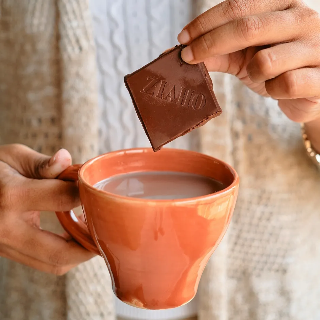 A person dipping chocolate into coffee to show how Indian chocolate brands like Ziaho are growing to offer the best dark chocolate India