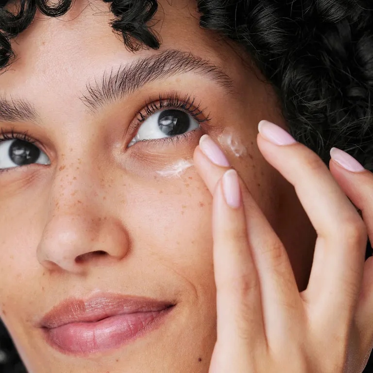 A woman look slightly upwards and applying the best under eye cream with her ring finger