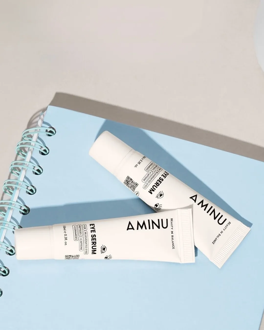 Two tubes of the best under eye cream for puffiness from Aminu placed on a blue book
