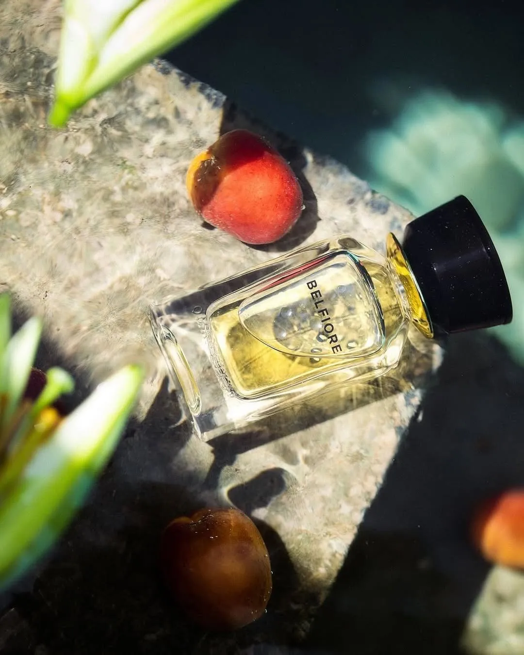 A bottle of perfume placed in a natural backdrop alongside a peach
