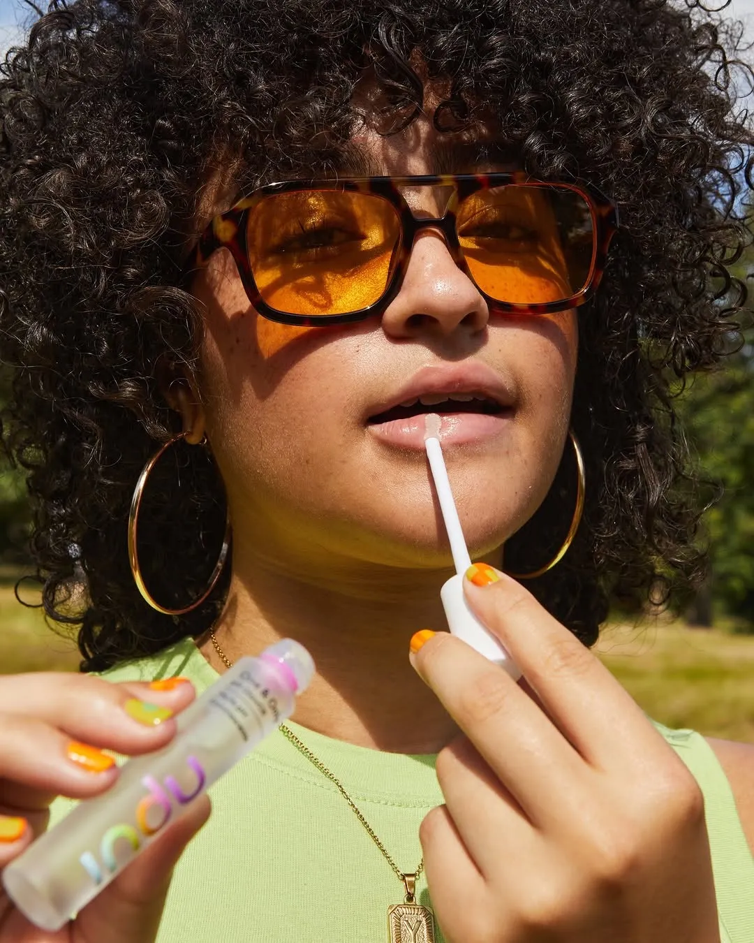A Gen Alpha girl with sunglasses applying a lip gloss, indicating a rise in Gen Alpha beauty consumption
