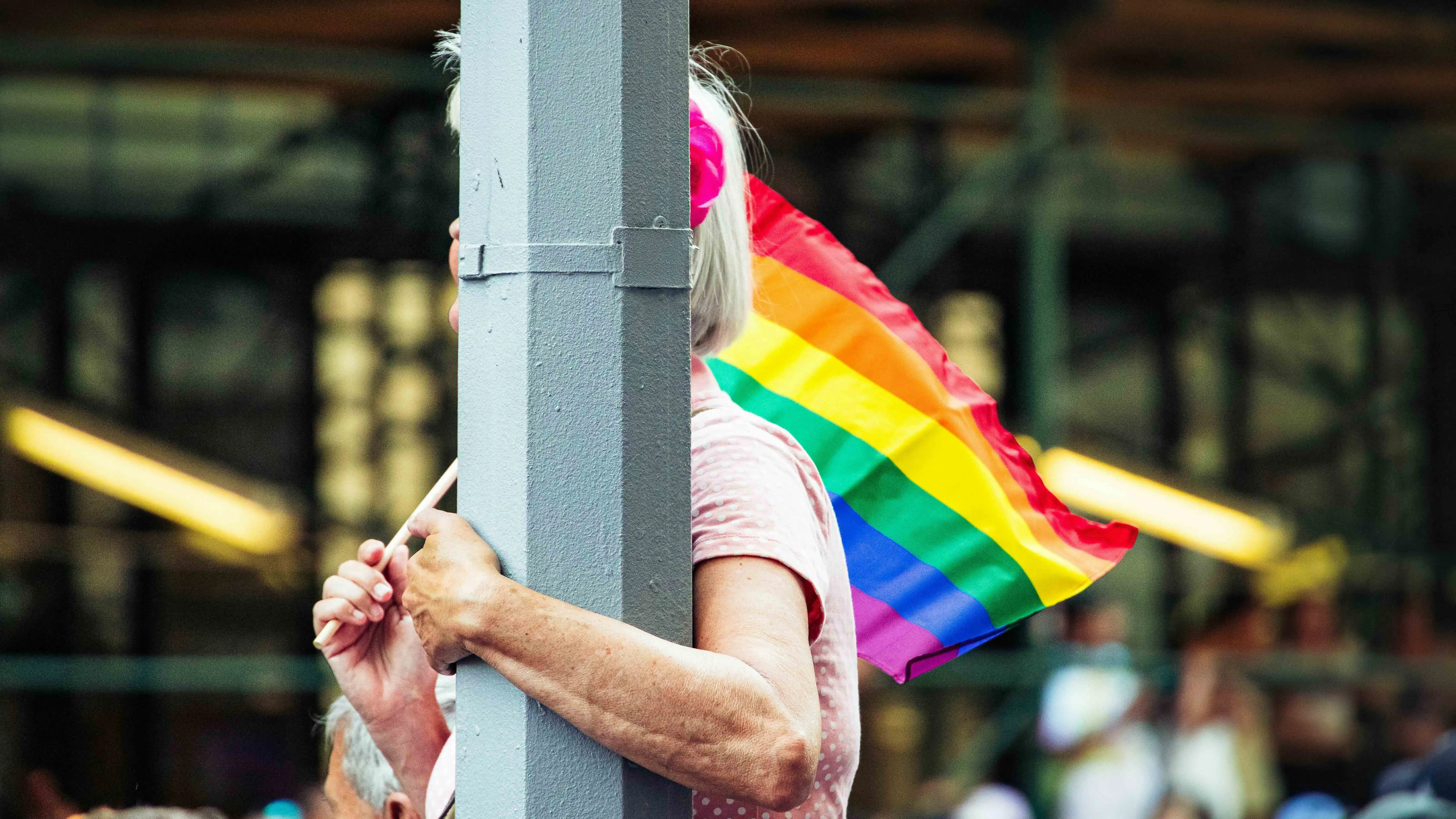 A person hugging a pole at a pride parade to show queer ageing in India, loneliness among queer elders and queer elder care India