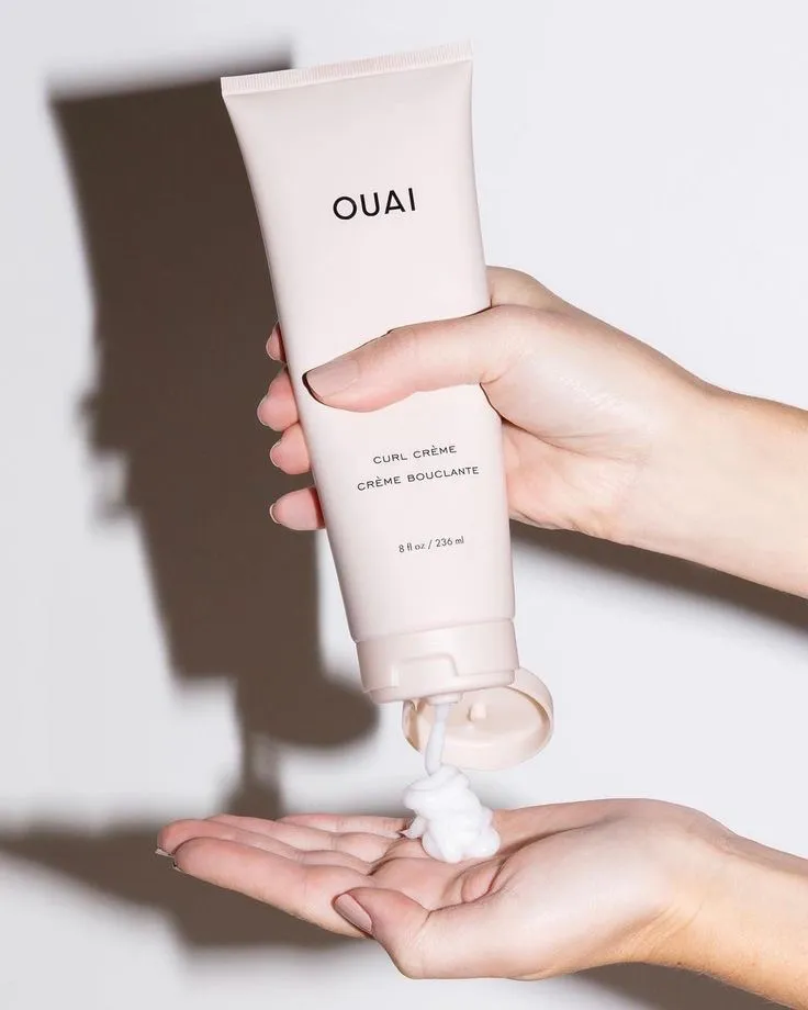 A bottle of curl creme from OUAI squeezed out in the hand