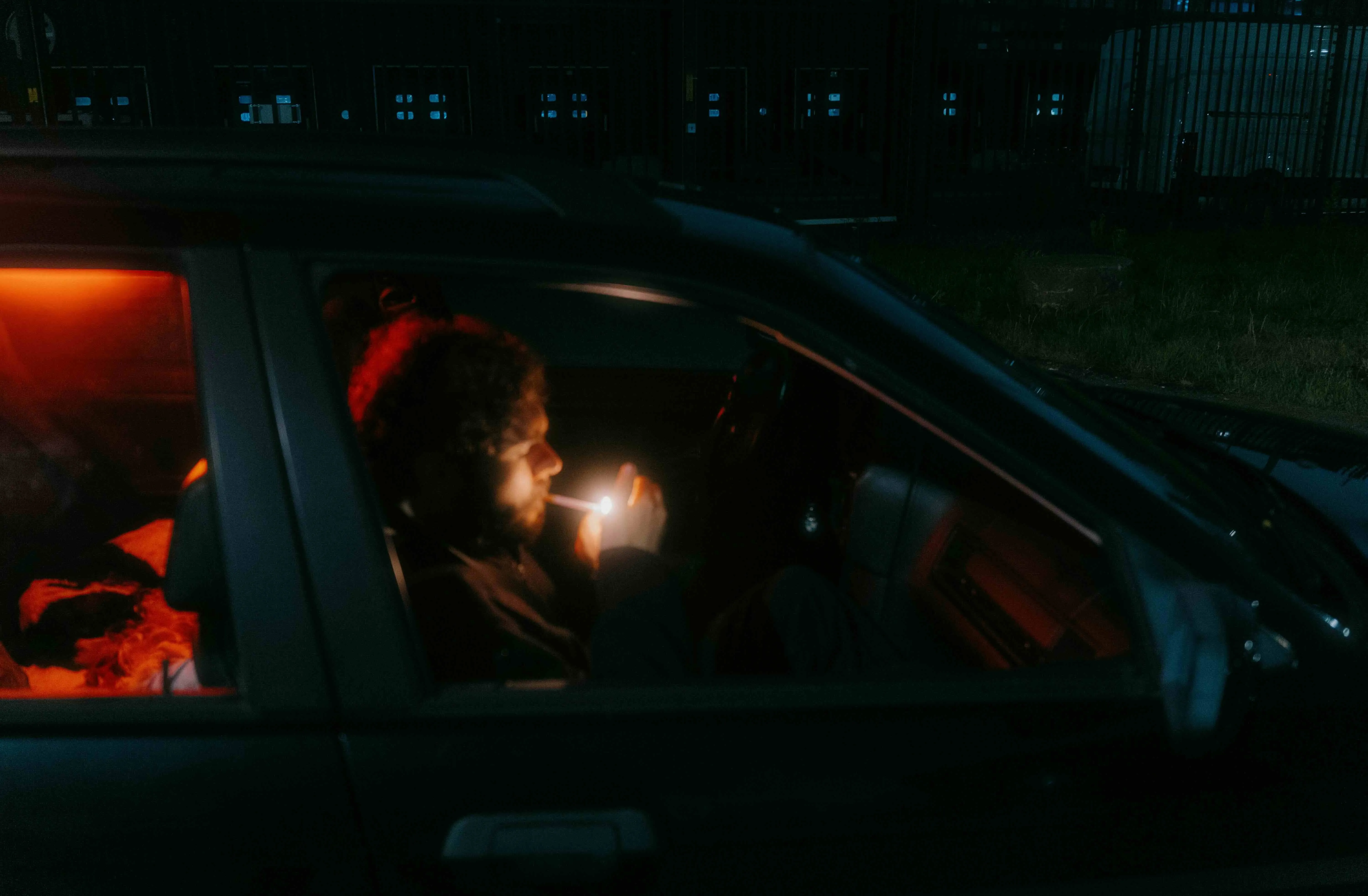 A man sitting in the car at night and smoking a cigarette