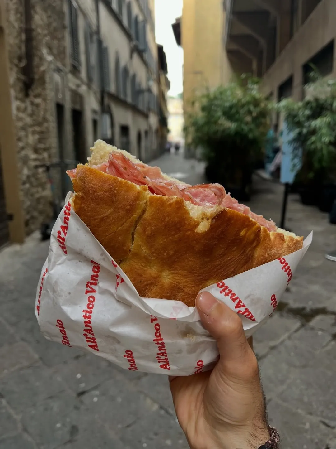 Traditional Italian schiacciata sandwich with cured meat, held outdoors on a Florence street